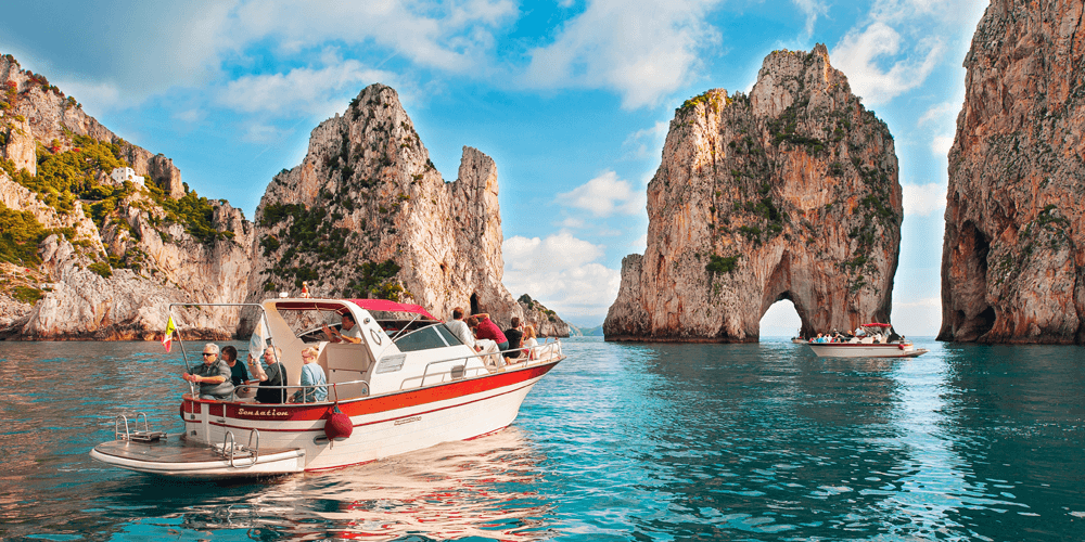 Boat cruising turquoise waters by Capri Faraglioni sea stacks