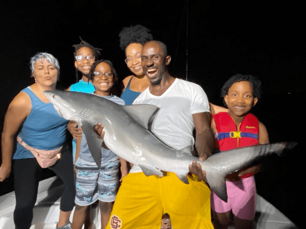 Family crew holding a freshly caught shark on a night fishing charter boat
