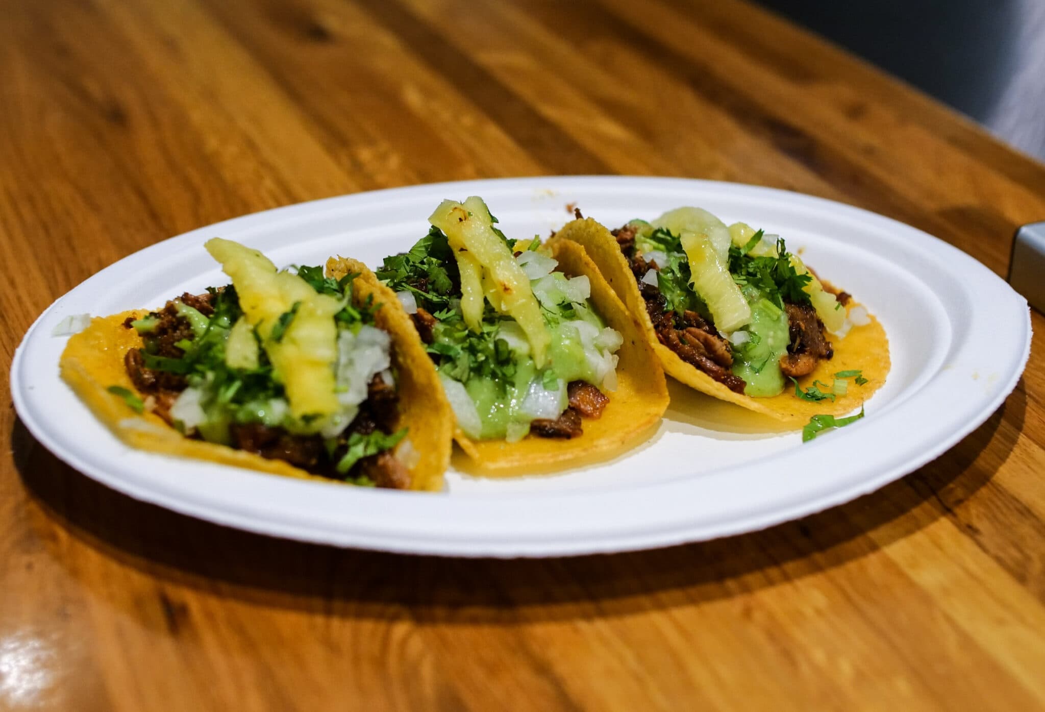 Three tacos on a plate on wooden table, casual street dining