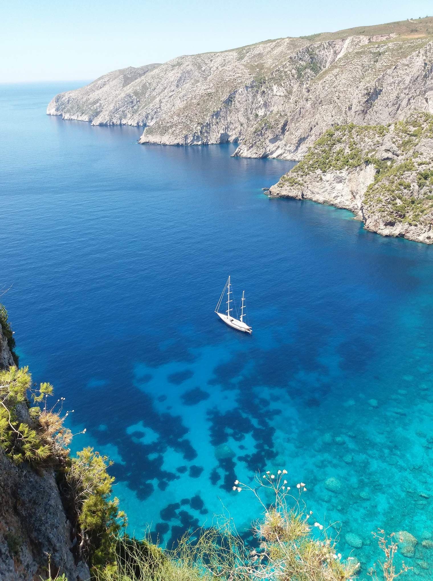 High cliff coastal vista overlooking sailboat in blue sea