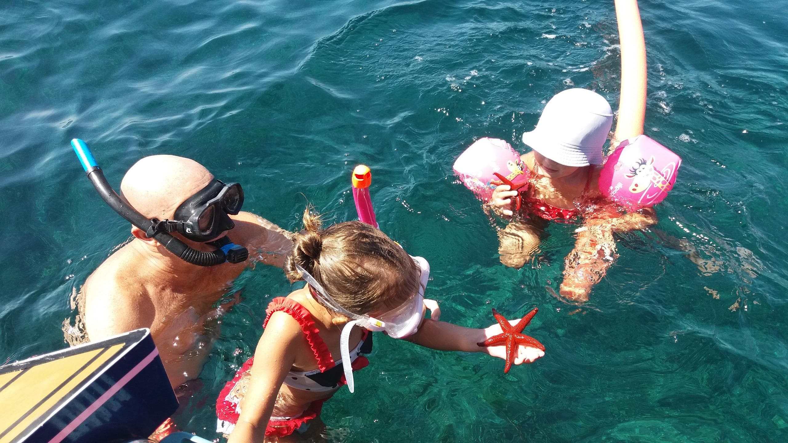 Family snorkeling and floating near boat in crystal coastal waters