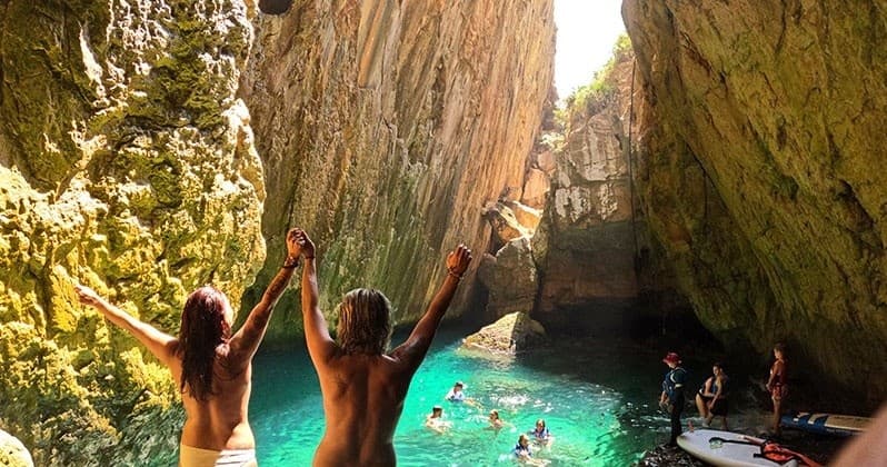 Swimmers exploring turquoise sea cave with raised arms and joy