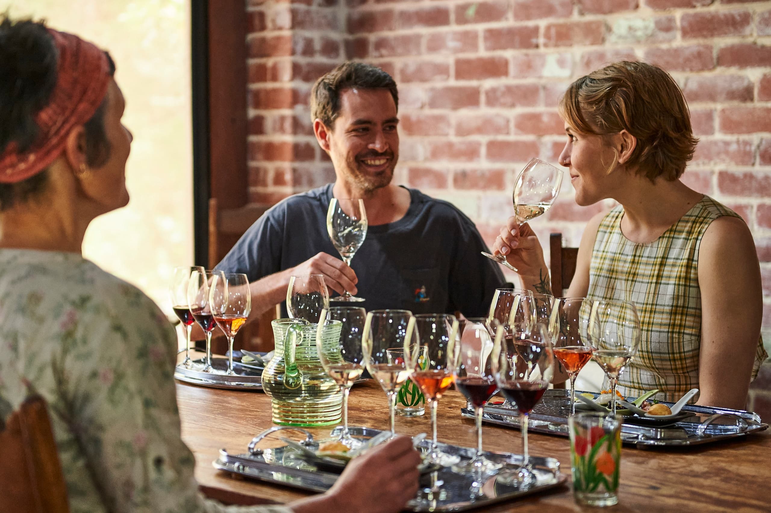 Friends tasting multiple wines at rustic winery communal tasting table