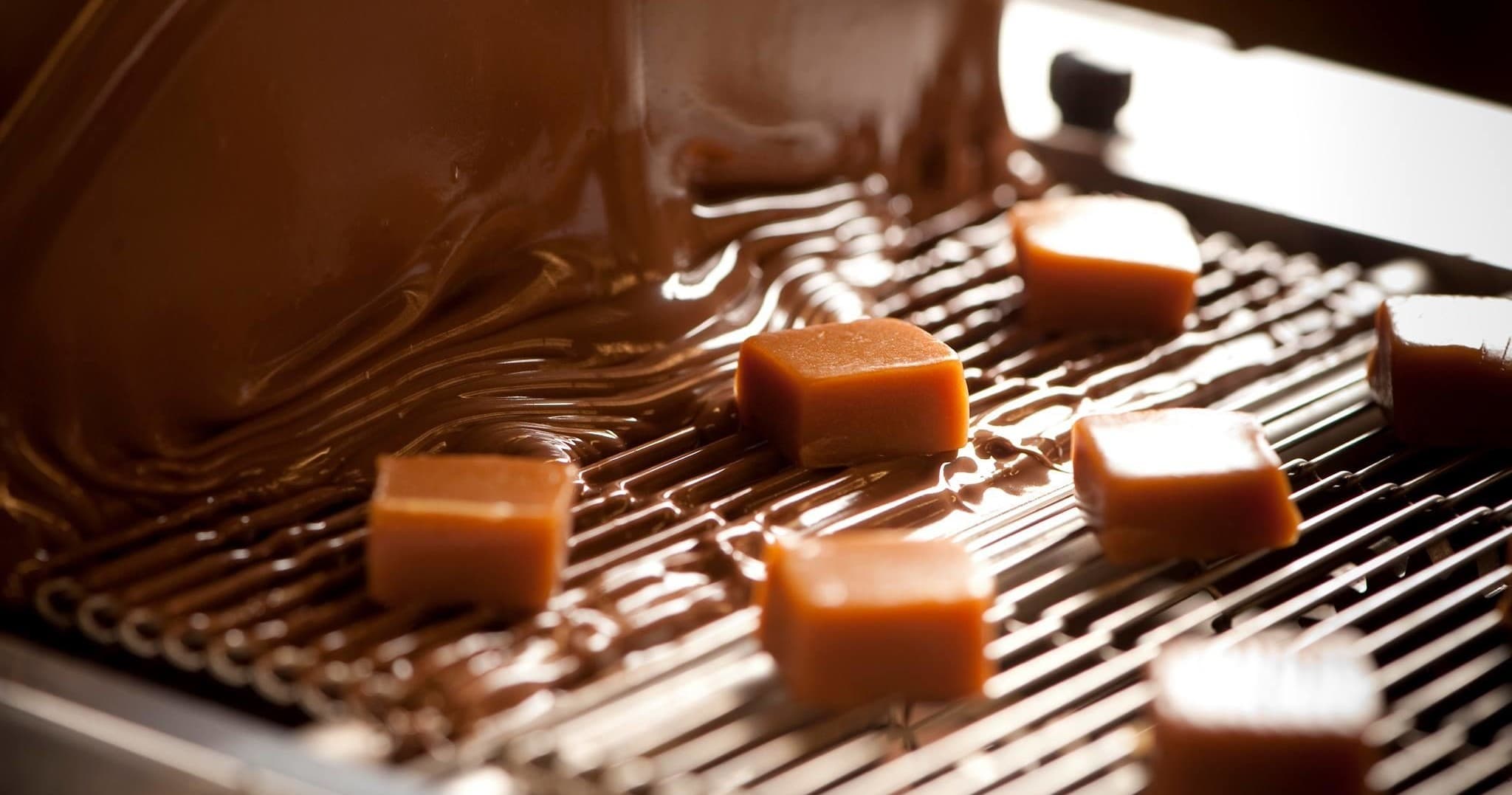 Caramels being enrobed in flowing dark chocolate in a chocolatier
