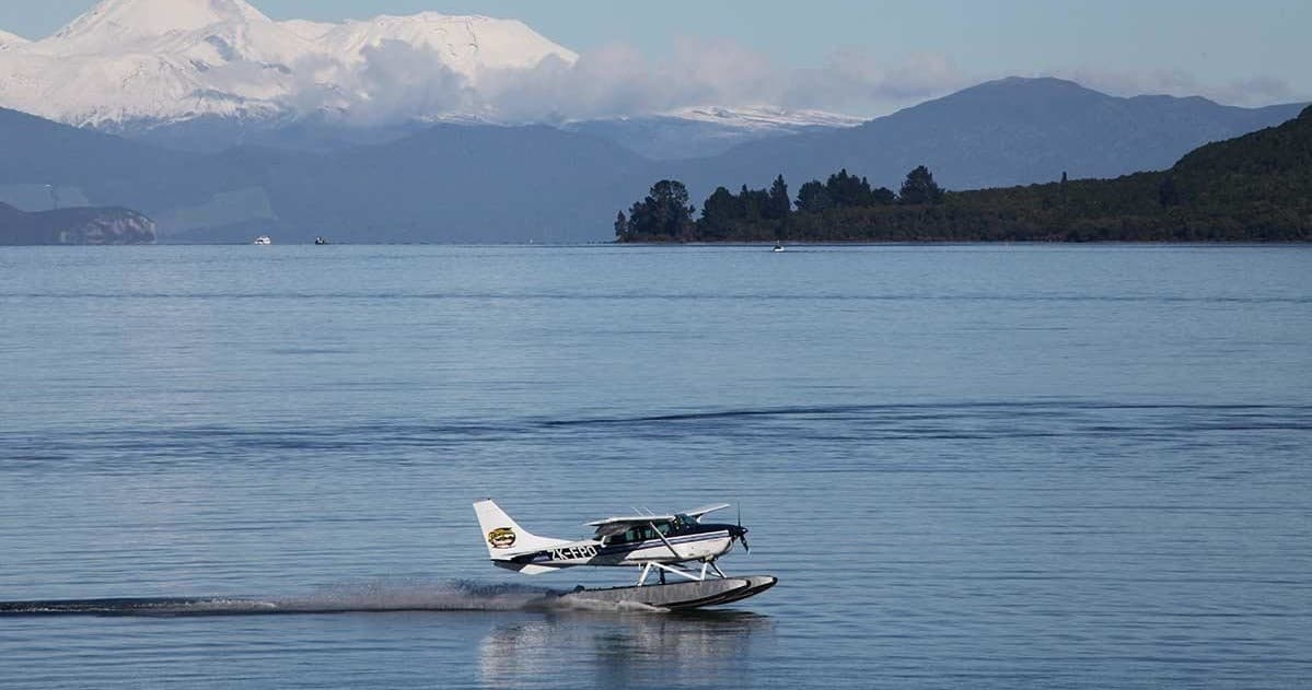 Seaplane taxiing on calm lake with distant mountains, scenic flight