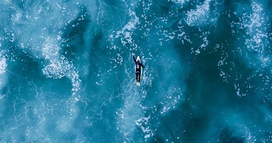 Aerial view of lone surfer paddling through deep blue ocean
