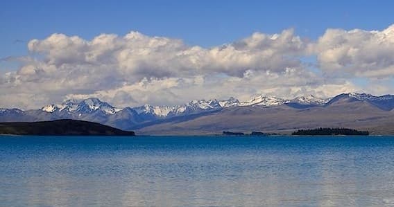 Turquoise alpine lake with distant snow peaks under blue sky