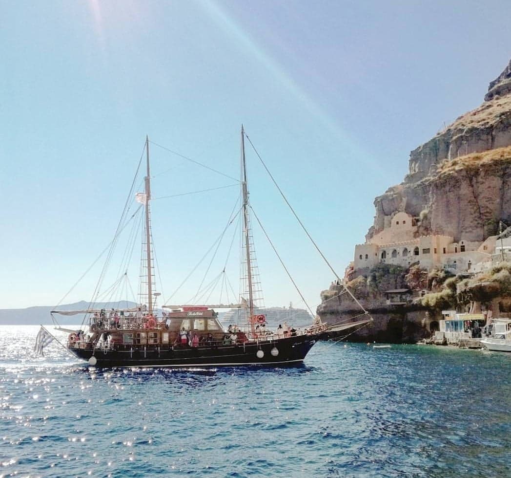 Sailing boat anchored by Santorini harbor with sunlit cliff houses