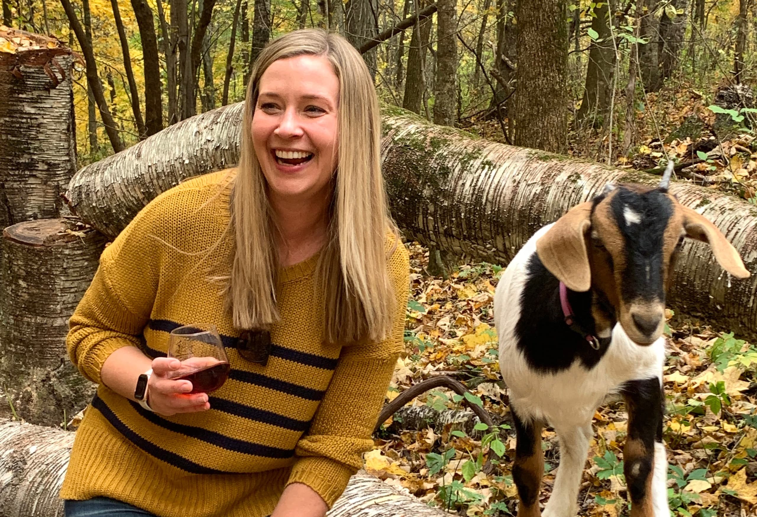 Woman laughing with goat on wooded trail during goat trek