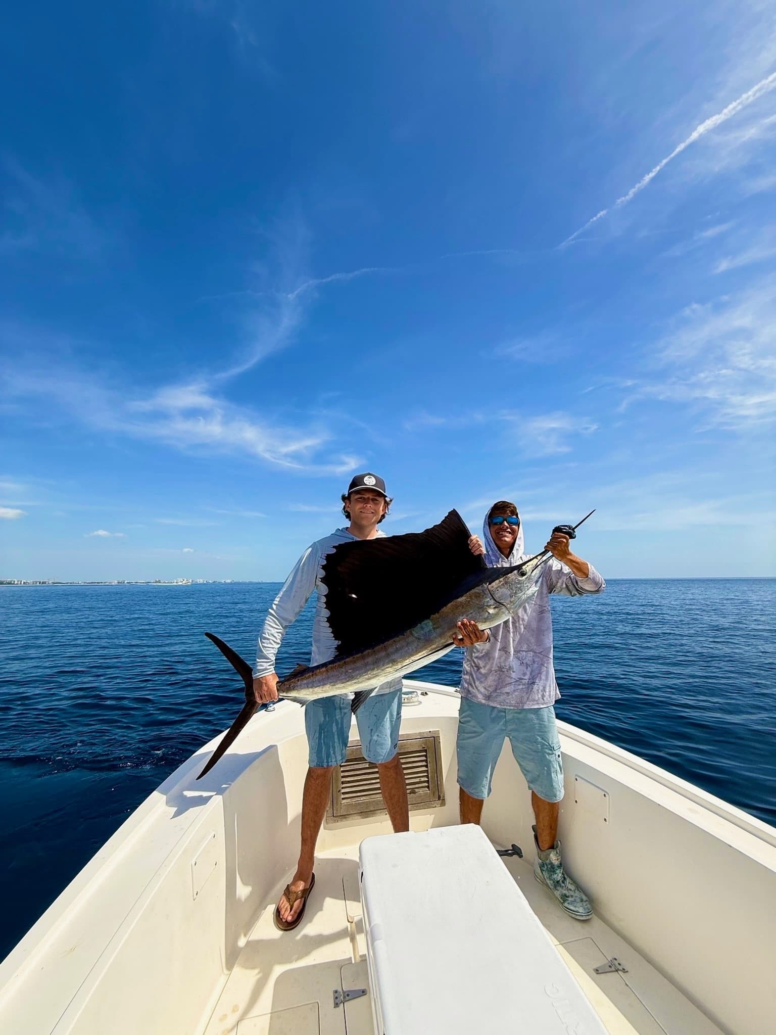 Two anglers holding large sailfish on boat, open ocean fishing