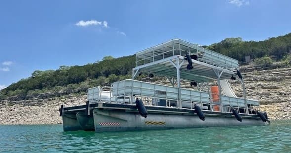 Double-deck pontoon boat anchored near rocky shoreline for lake party
