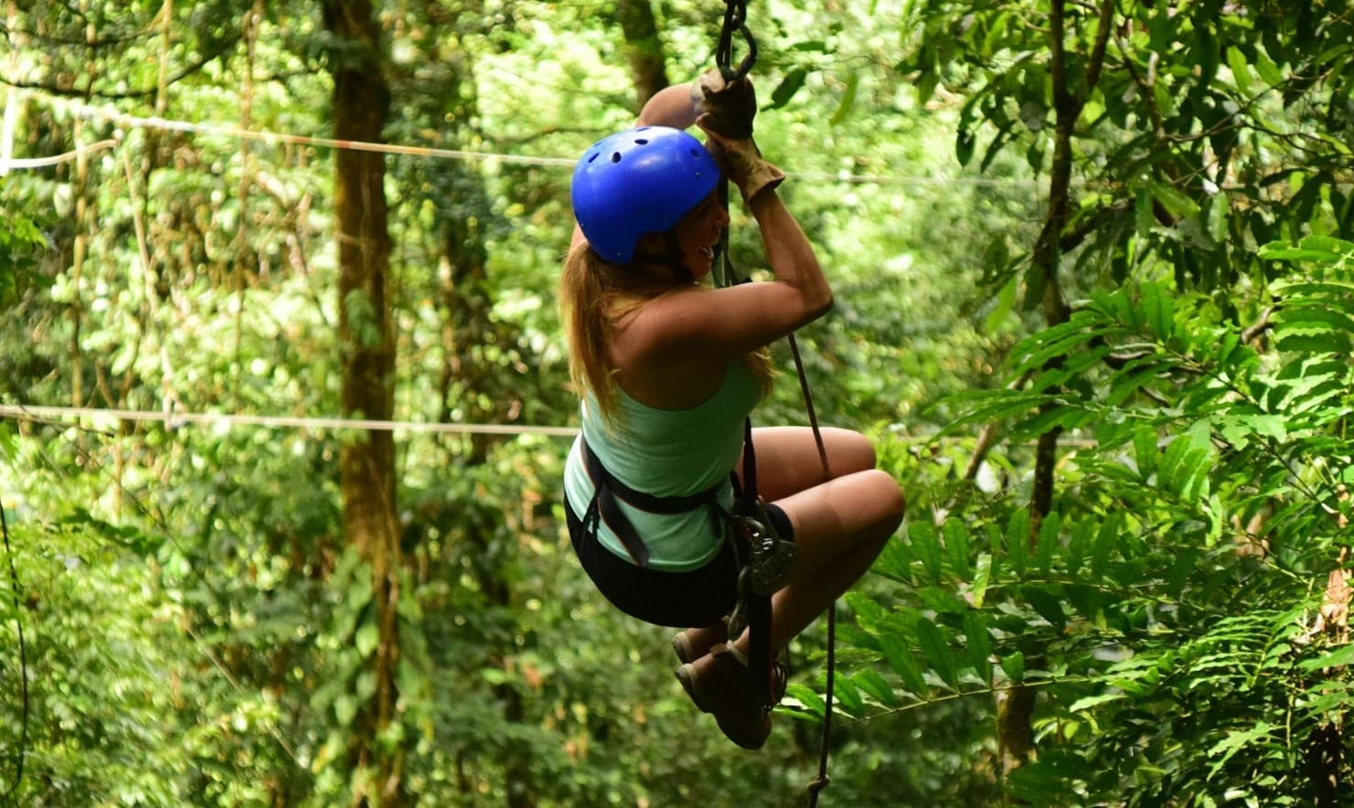 Adventurer ziplining between treetops over lush tropical forest