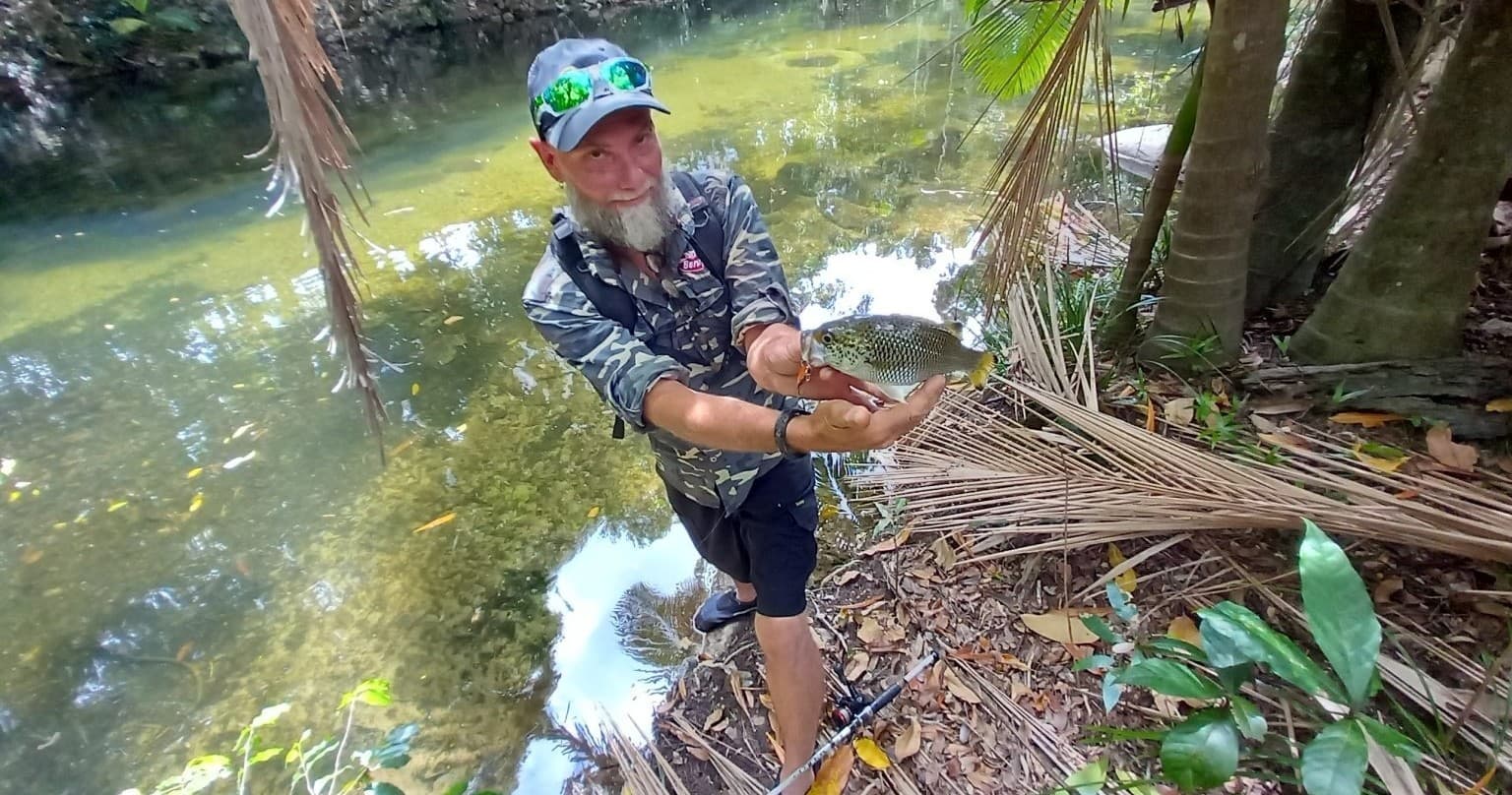 Fisherman holding small freshwater fish beside jungle creek