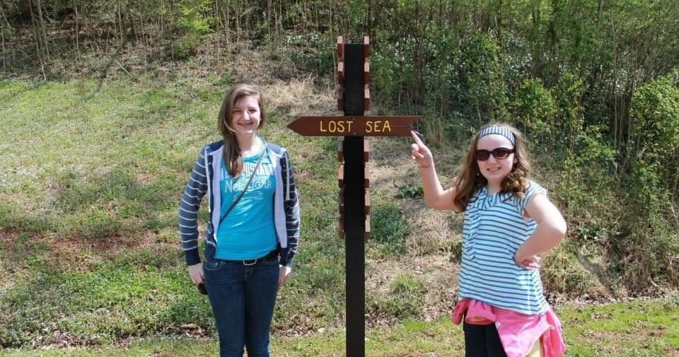 Visitors posing at Lost Sea trail sign near forested roadside entrance
