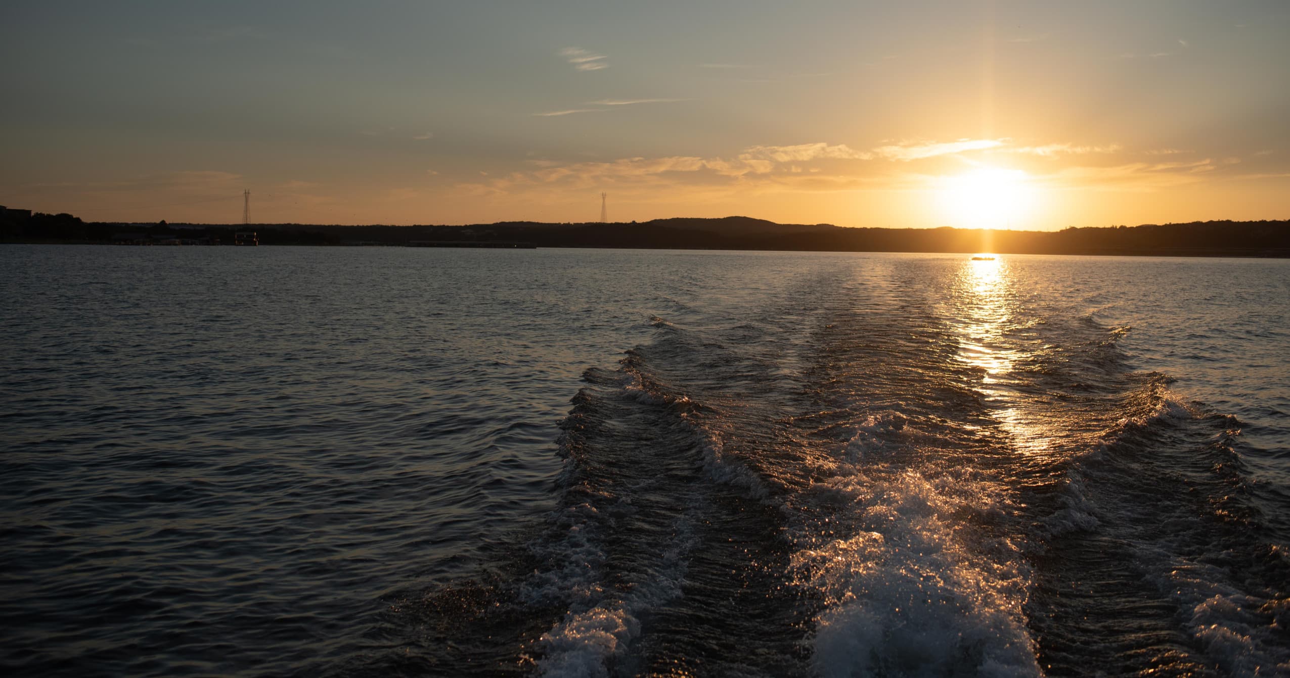 Boat wake cutting through sunset waters on a scenic lake
