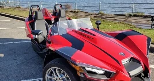 Red Slingshot parked by waterfront promenade showcasing coastal drive