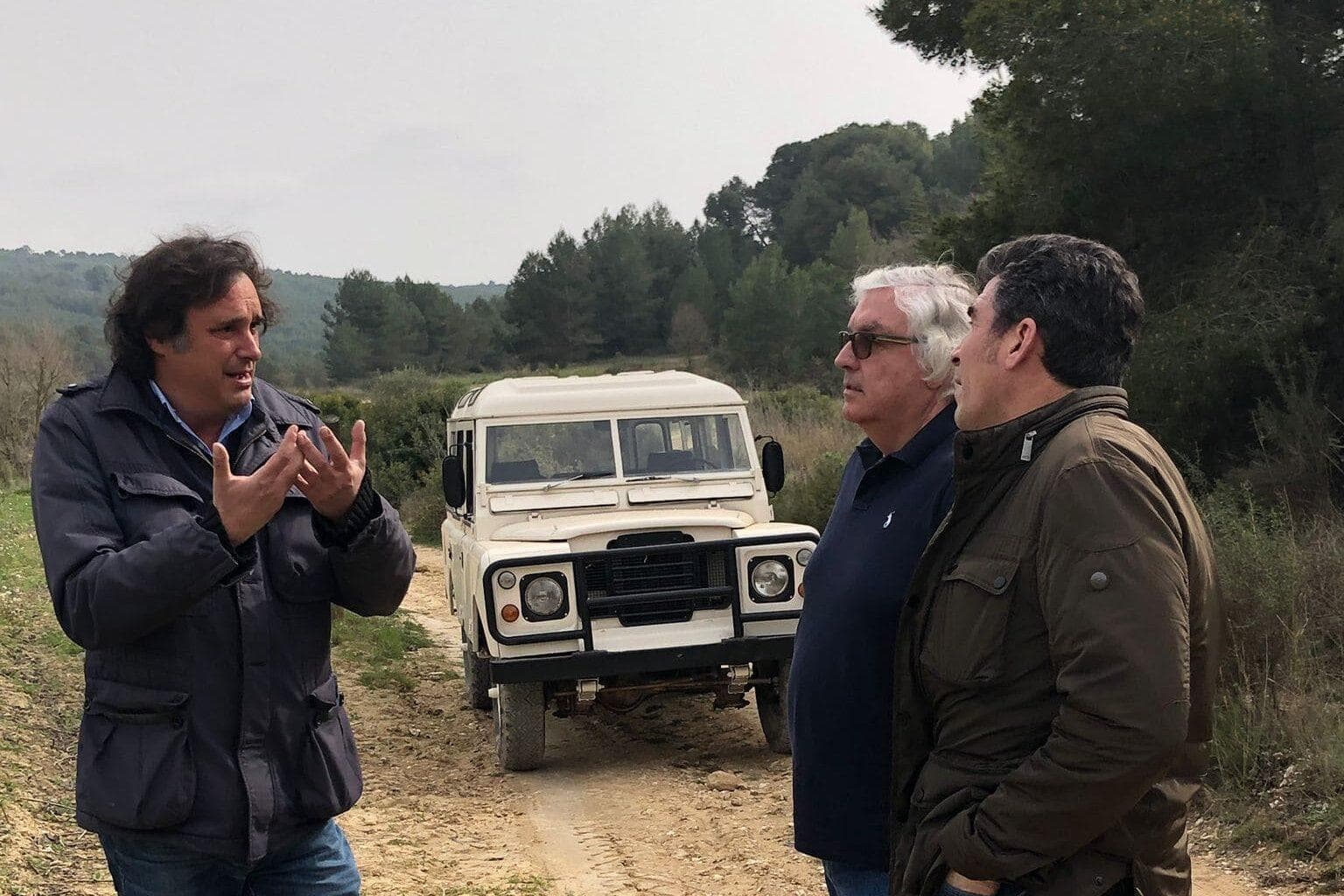 Three men discussing off-road route beside a 4x4 on dirt track
