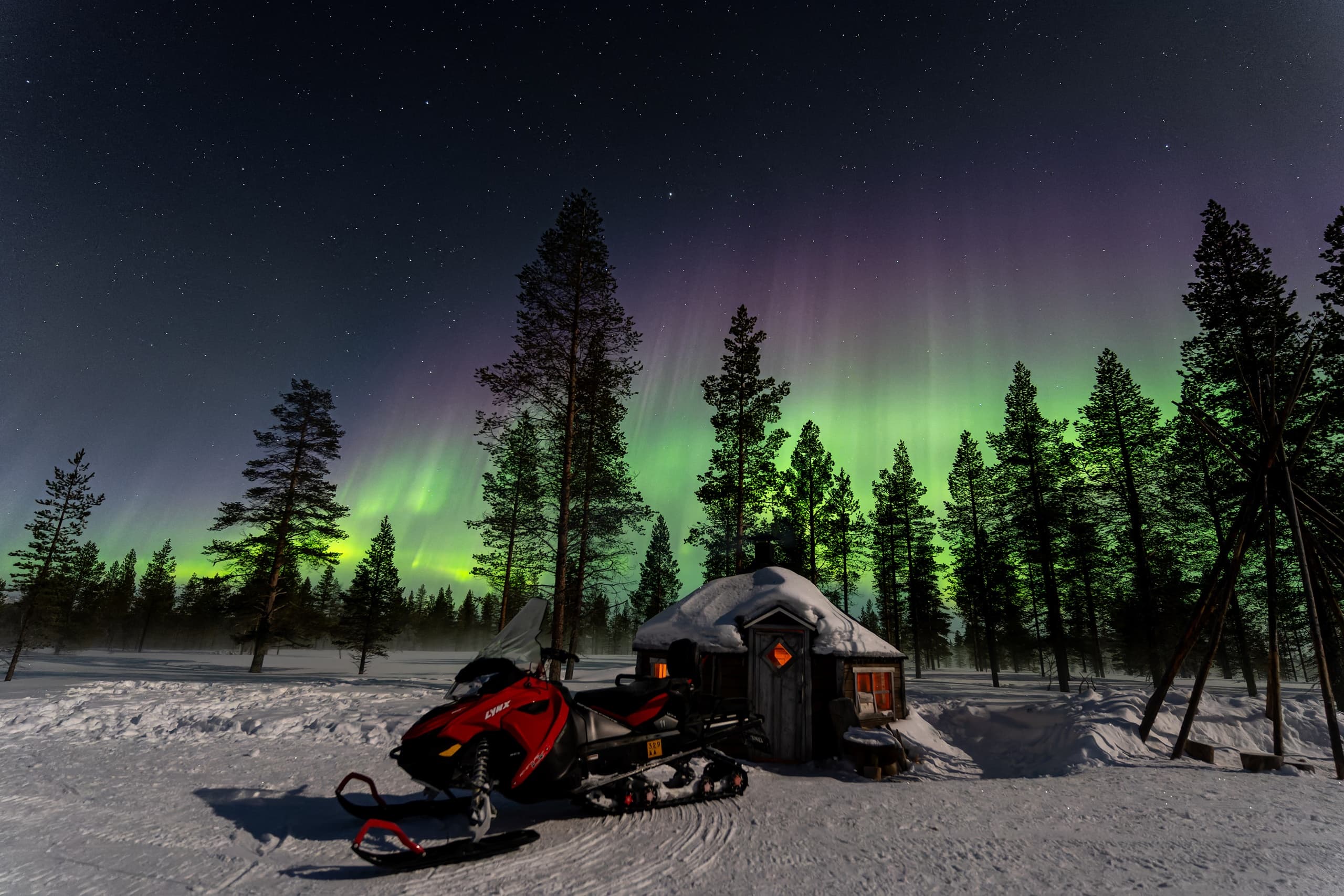 Aurora borealis above snowmobile and cabin in Saariselkä wilderness