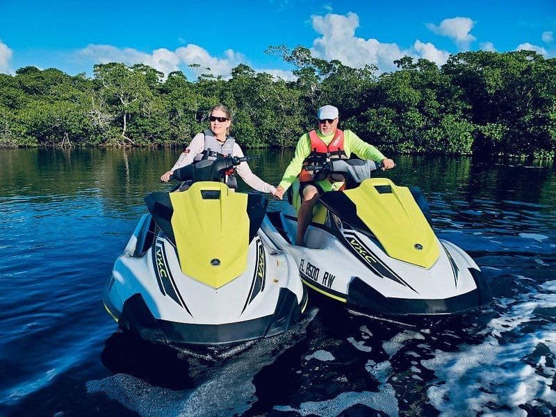 Two riders on jet skis cruising mangrove-lined coastal waters