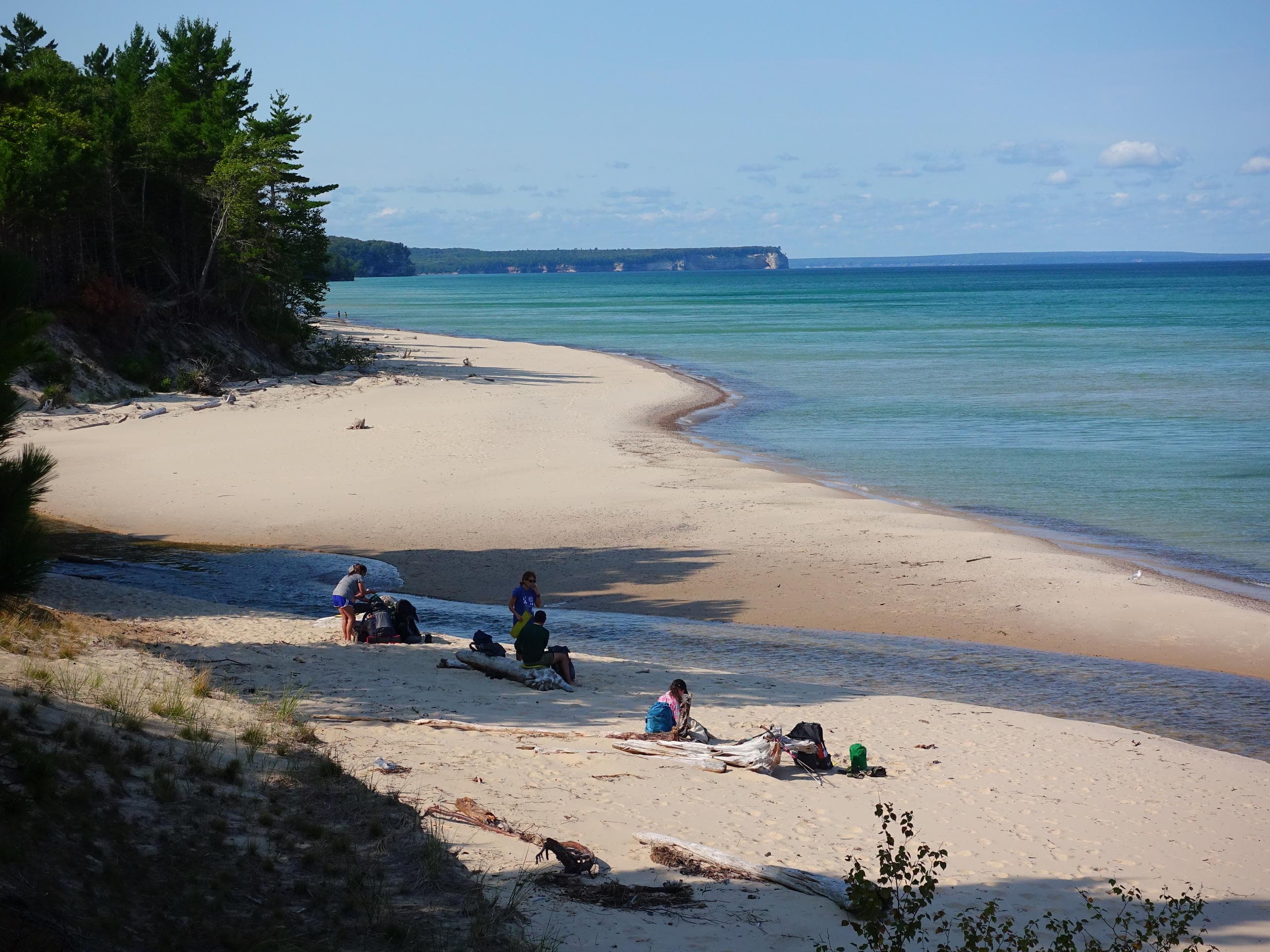 Campers relaxing on sandy lakeshore with cliffs and clear water