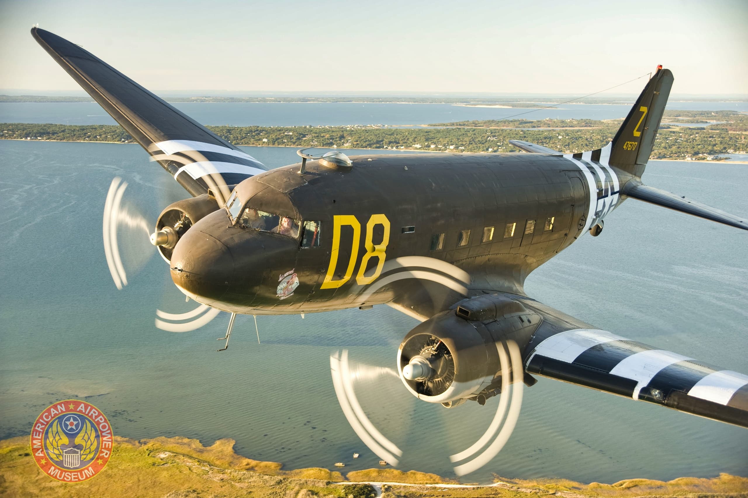 Vintage C-47 transport flying over coastline with scenic views