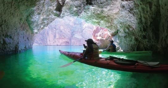 Kayakers silhouetted inside turquoise canyon cave paddling