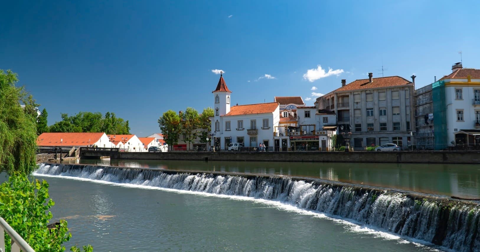 Riverfront town with cascading weir in Portugal, scenic view