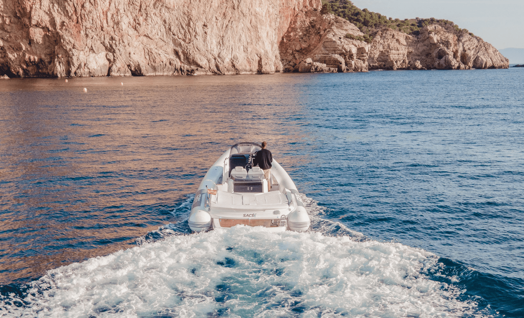 Speedboat heading toward sunlit cliffs, coastal sunset boating view
