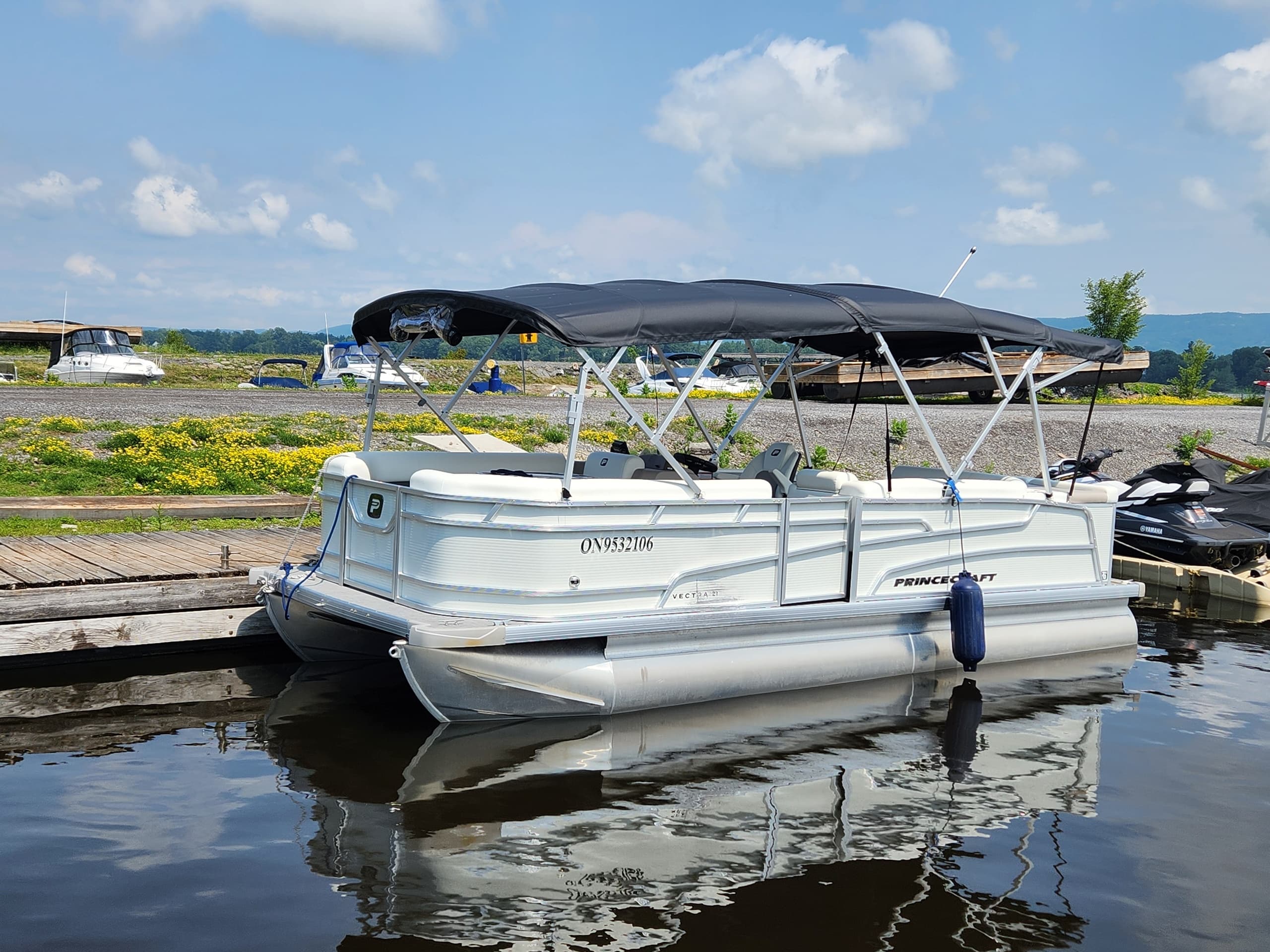 Docked pontoon boat reflecting on calm marina water, summer day