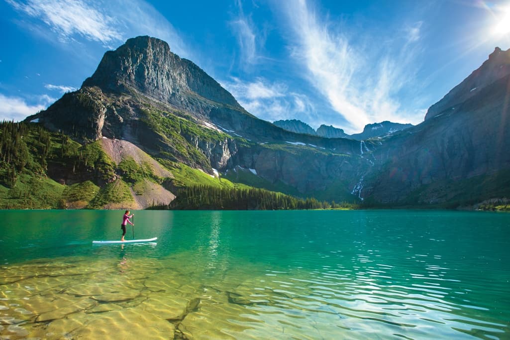 Paddleboarding across turquoise alpine lake beneath dramatic mountain peaks