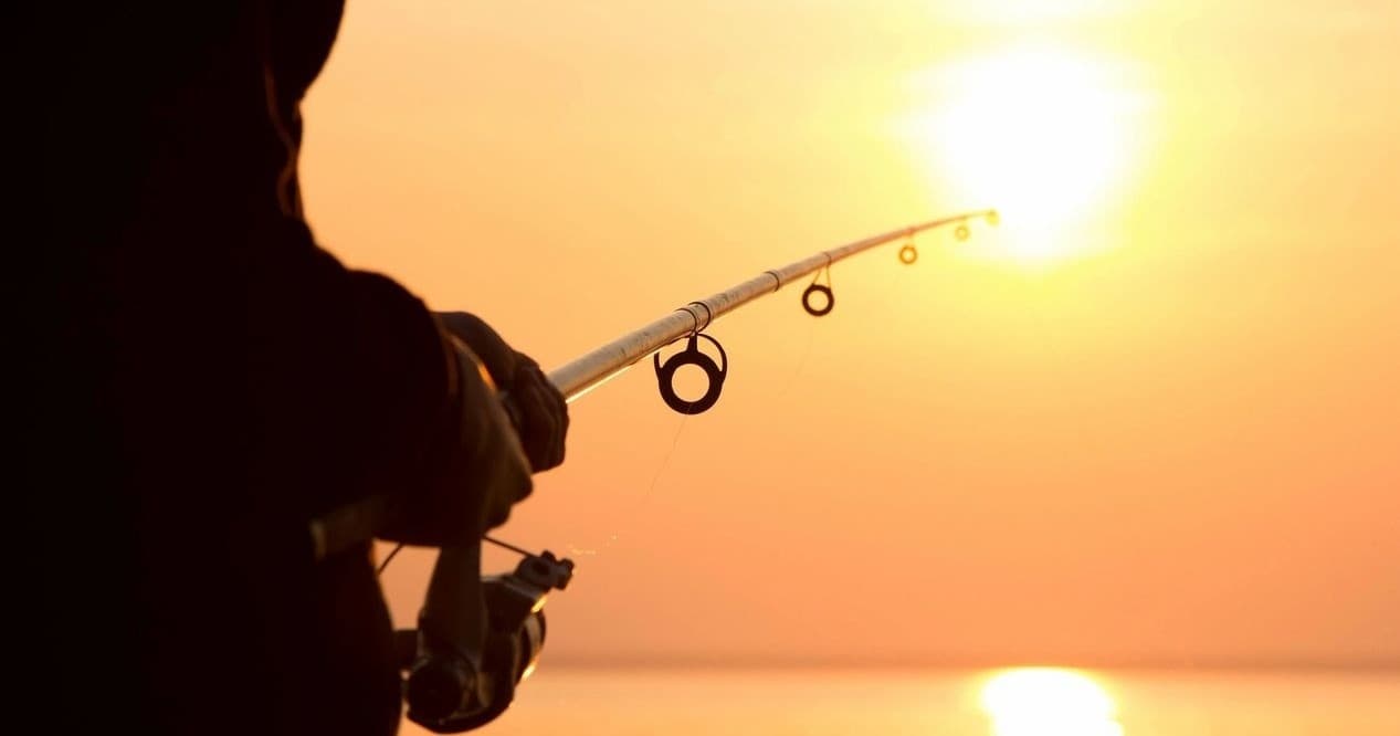 Angler casting at sunset over open ocean with golden sky