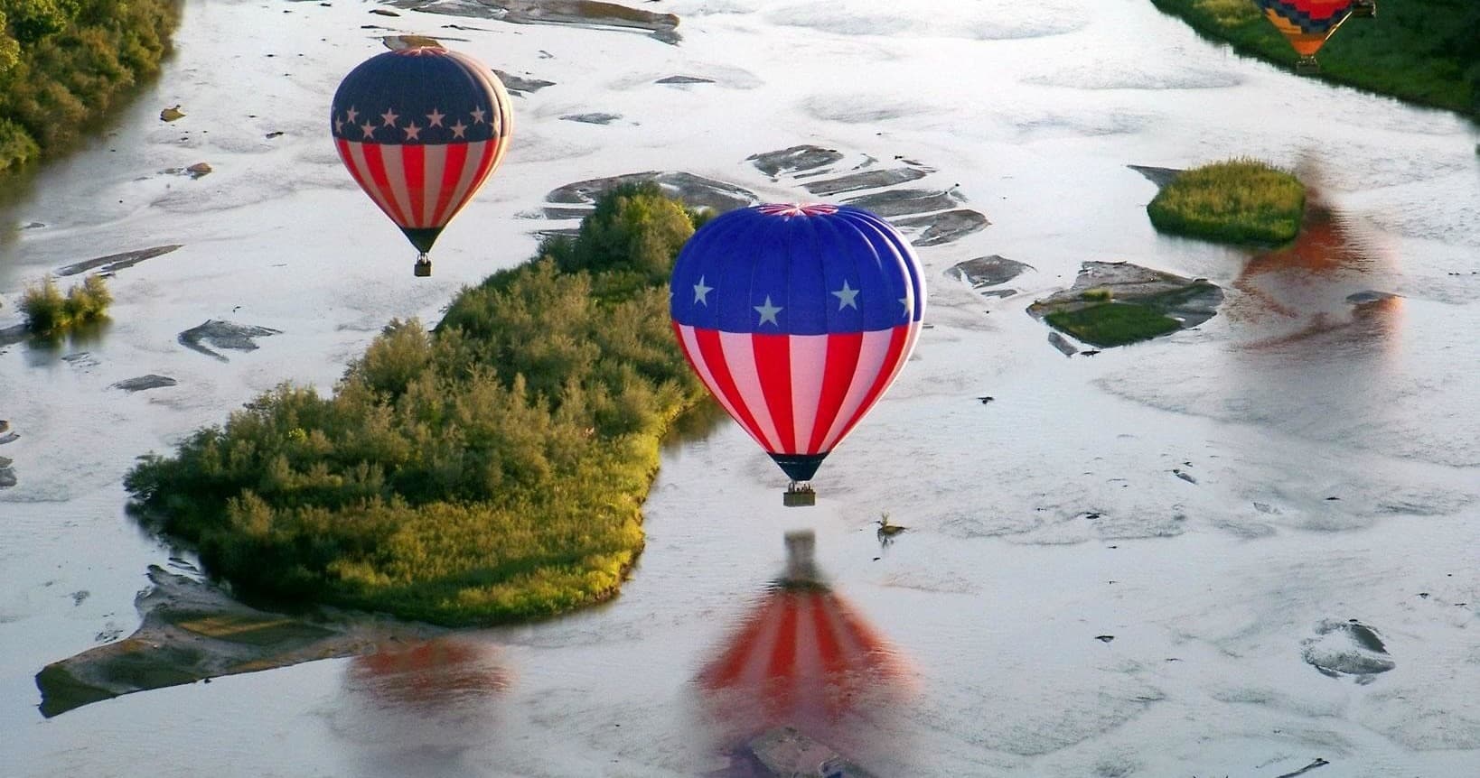 American patterned hot air balloons over tidal wetlands reflecting sky