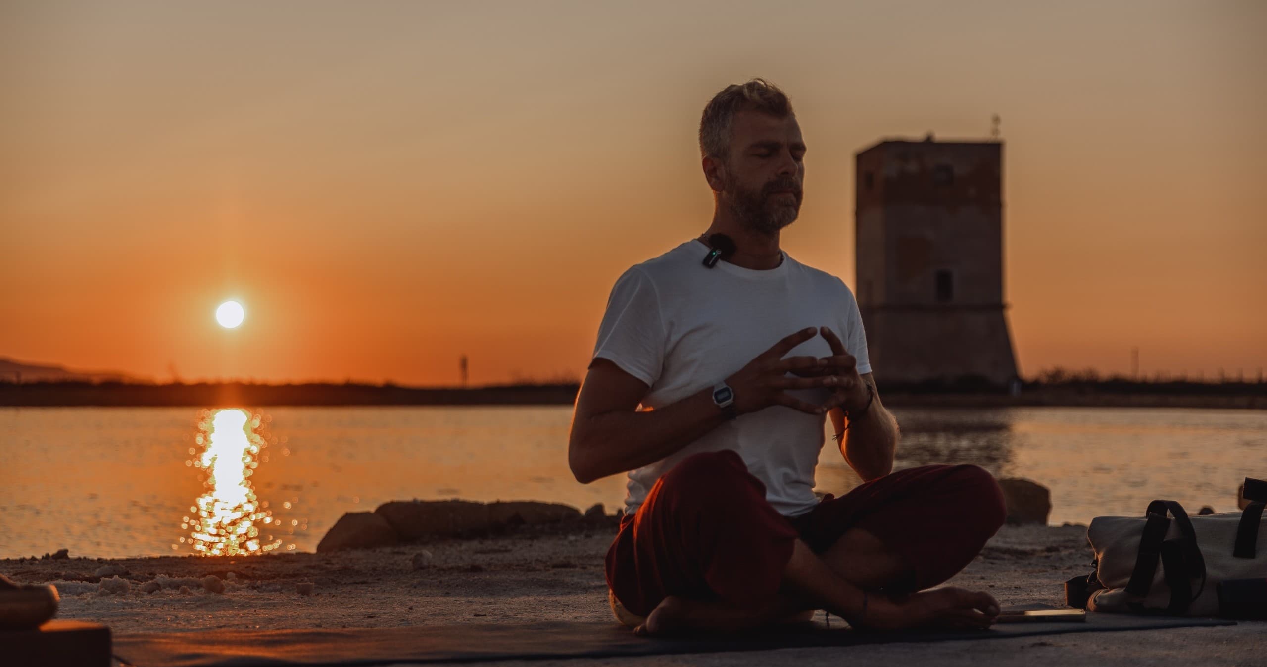 Man meditating at sunset by coastal lagoon with tower