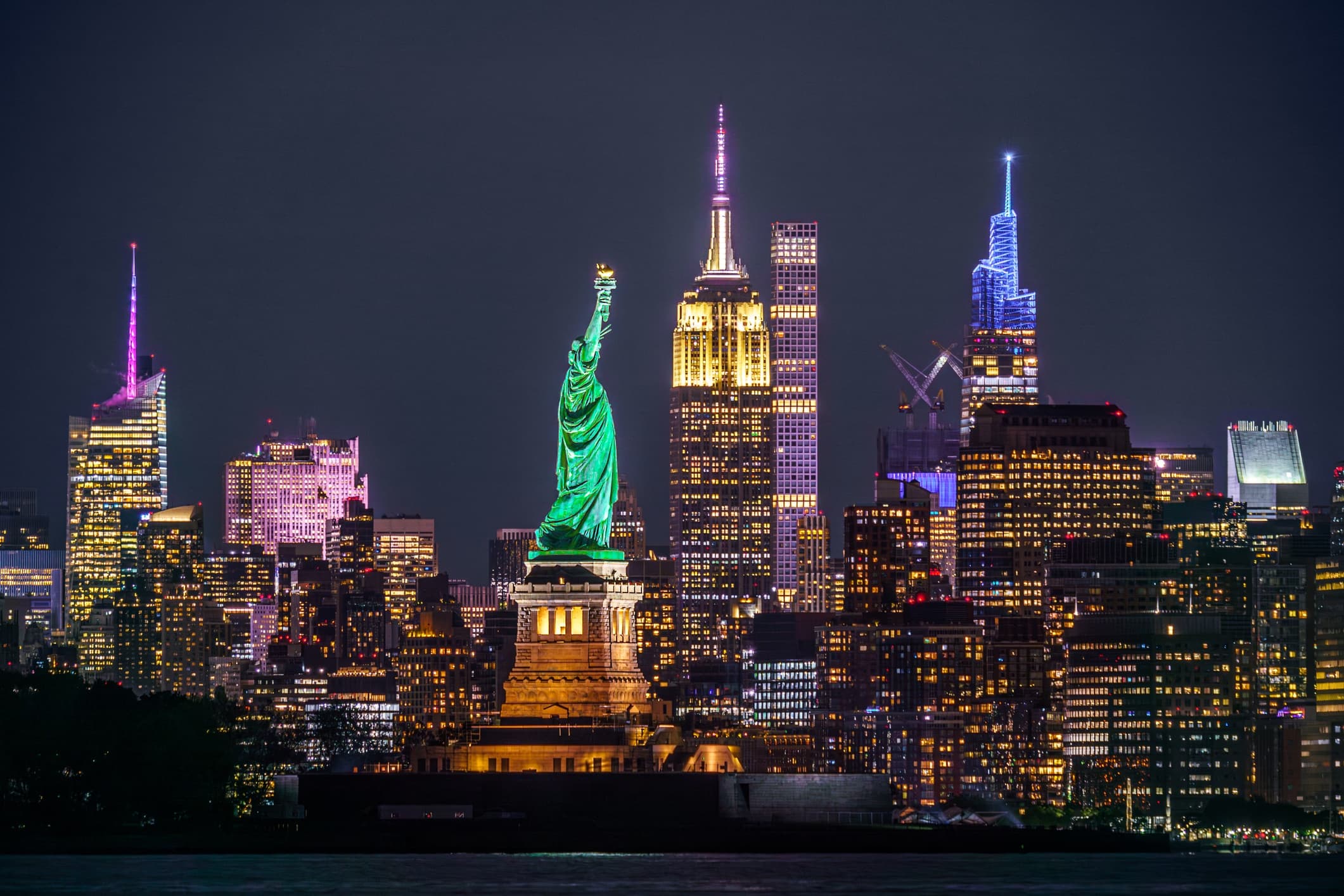 Night Manhattan skyline with Statue of Liberty lit, harbor sightseeing view