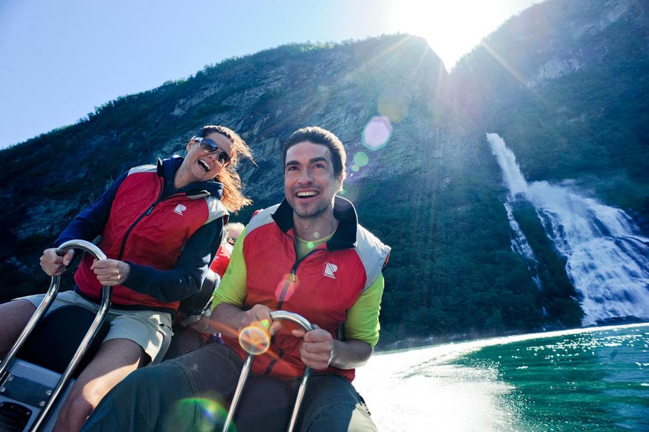 Couple kayaking in sunny fjord waters near cascading waterfall