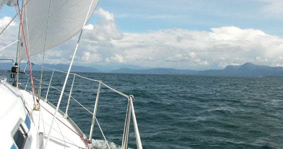 Sailboat cruising on open sea with distant coastal mountains