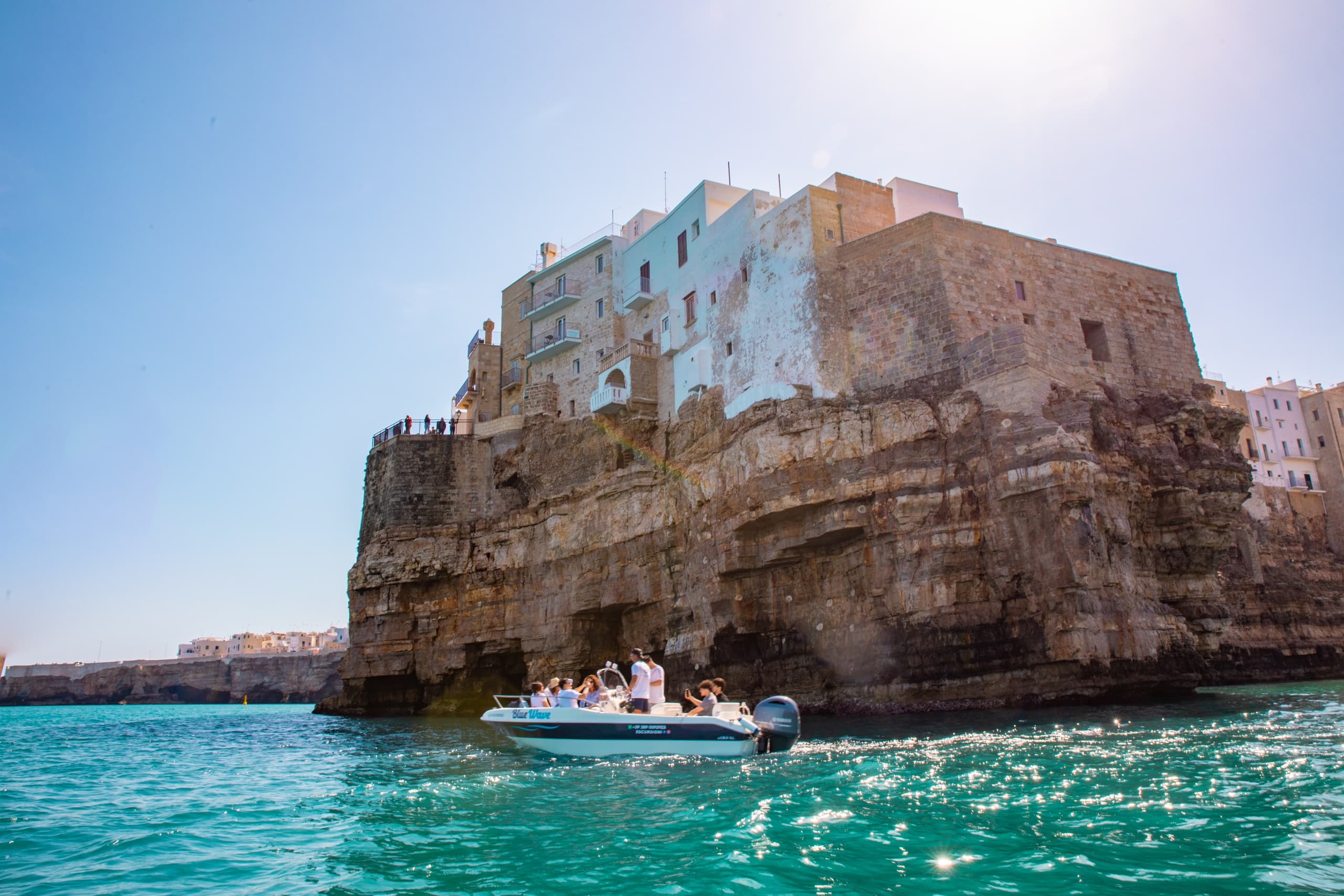 Boat cruising past cliffside town on turquoise Mediterranean sea