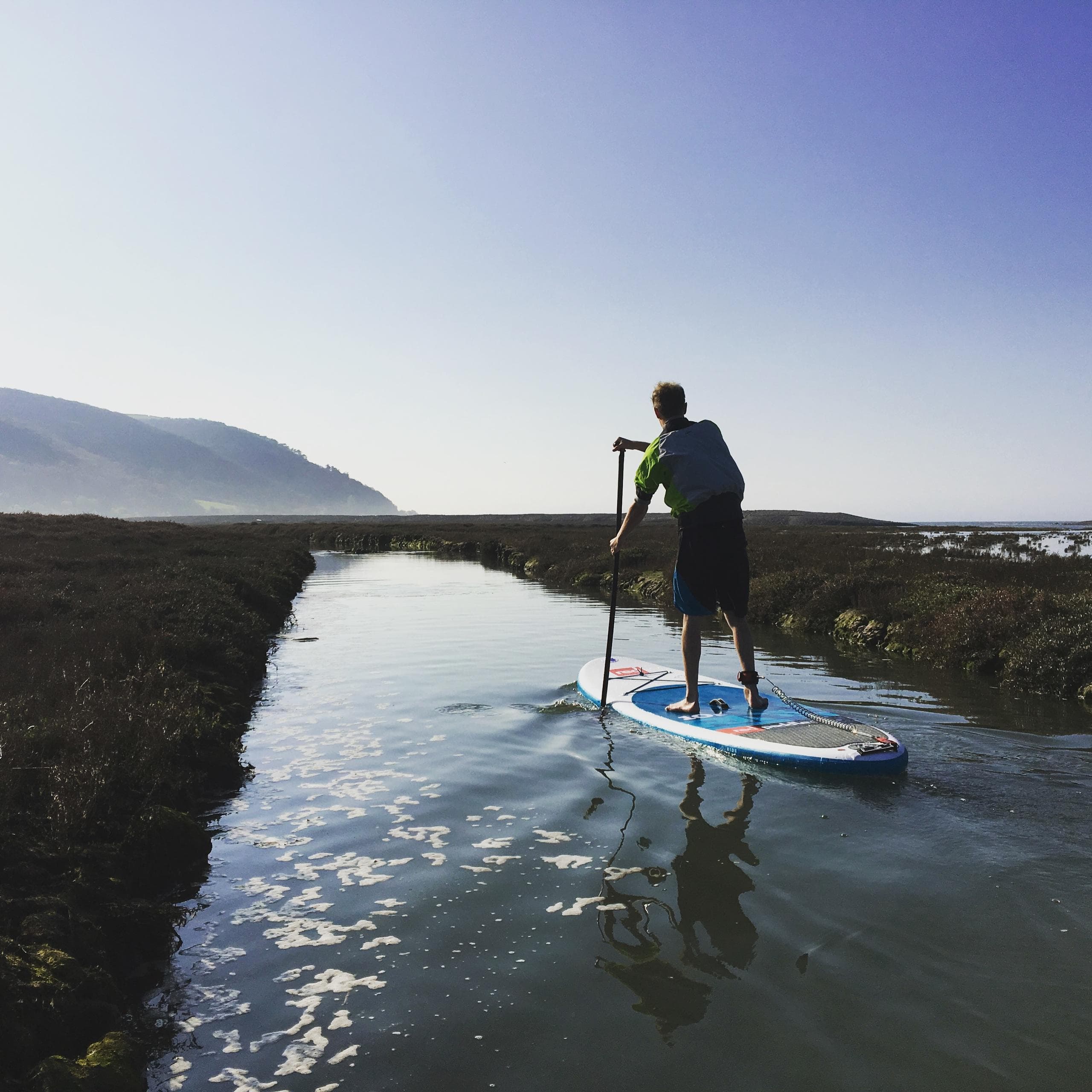 Stand-up paddleboarder gliding through coastal estuary at dawn