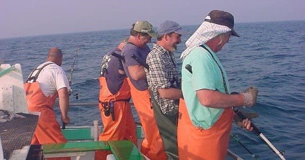 Crew hauling fishing lines on charter boat in open sea