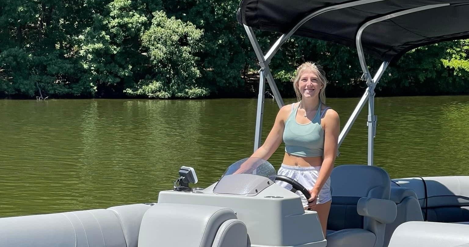 Person steering pontoon boat on peaceful lake under canopy