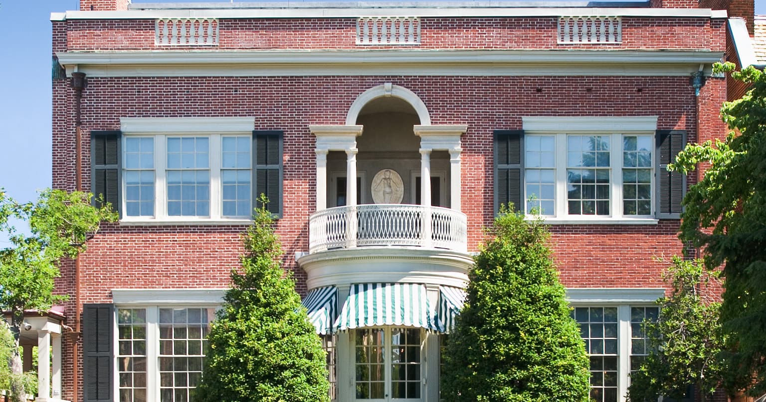 Red brick historic home facade with balcony and landscaped shrubs