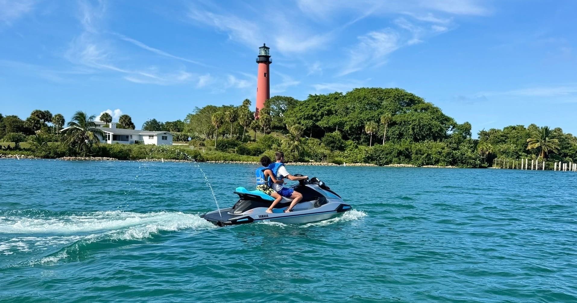 Jet ski riders near lighthouse on turquoise coastal waters