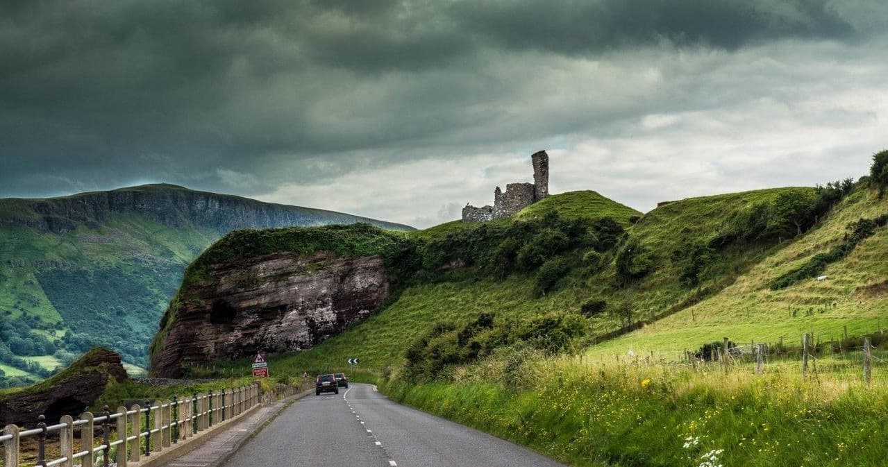 Scenic coastal road leading to medieval castle ruins in Irish countryside