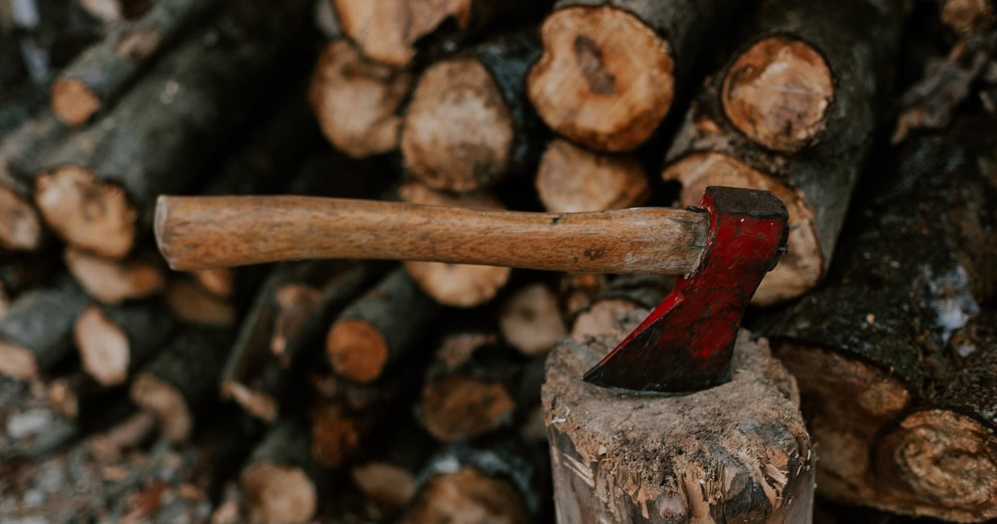 Red-bladed axe resting on chopped stump with woodpile backdrop
