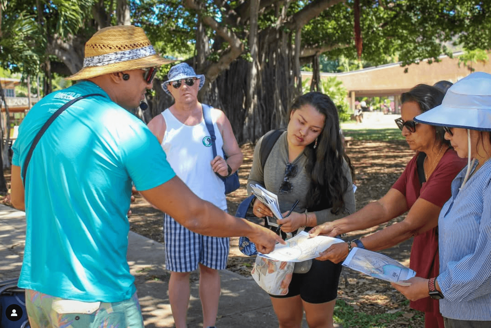 Guided walking tour participants exchanging maps under a banyan tree in park