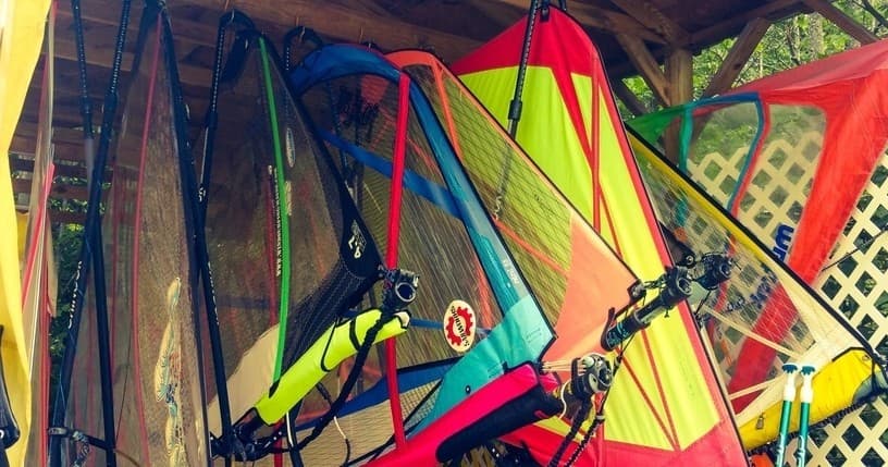 Colorful windsurf sails and rigs stored under lakeside shelter