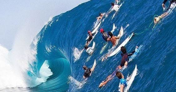 Surfers paddling into a towering blue ocean wave during lineup