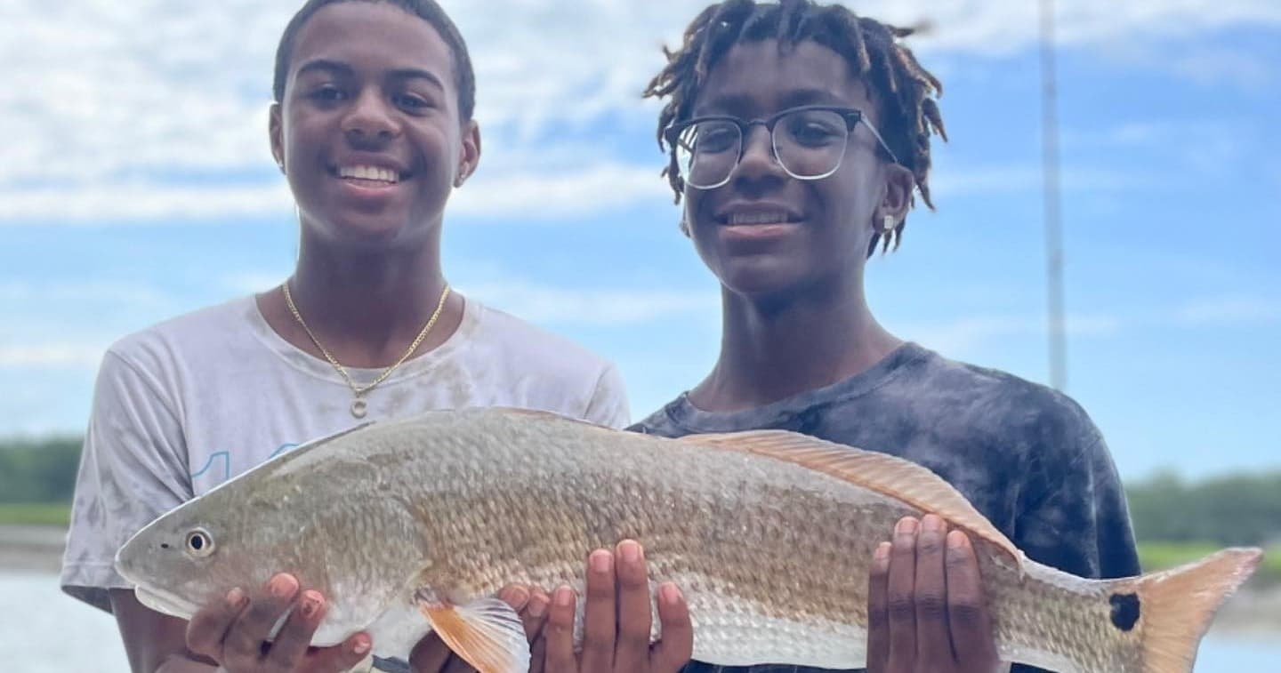 Two anglers holding large redfish on dockside marsh shoreline
