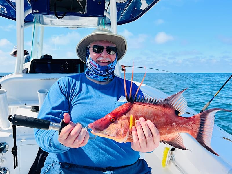 Angler holding colorful reef fish aboard boat with clear blue sea