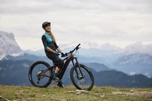 Solo rider climbing a forested mountain road with sunlight